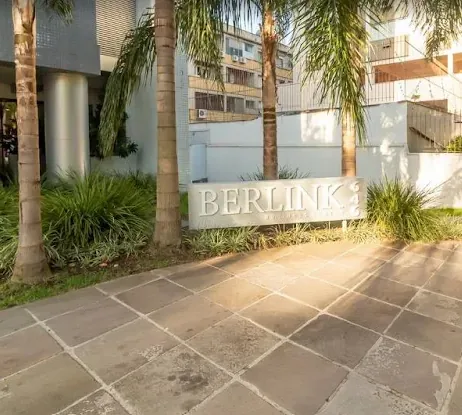 Entrada do Edifício Berlink Business Center, com o nome do prédio em letreiro sobre um muro baixo e jardim com palmeiras.