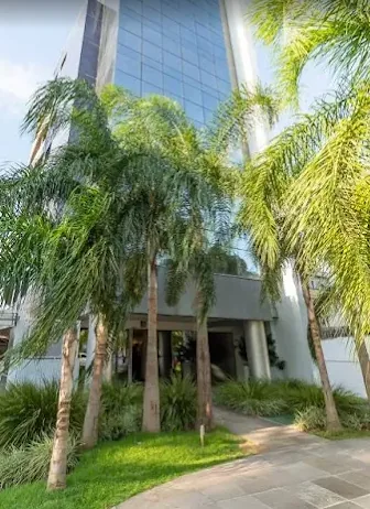 Torre envidraçada do Edifício Berlink Business Center, cercada por palmeiras, em Porto Alegre.